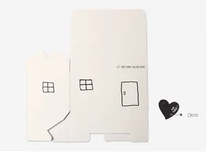 Flat lay view of a white house-shaped gift box template with heart tag and accessories