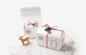 Close-up of house-shaped gift boxes with hand-drawn windows and red twine on lace mat