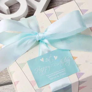 Nastro di raso blu lago su confezione regalo crema con motivi a bandierine per neonati