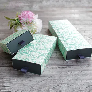 Three green damascus pattern drawer gift boxes with purple ribbon handles on wood
