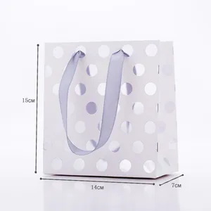 Detail view of small white gift bag with gold polka dots and purple ribbon handles