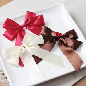 Three satin ribbon bows in burgundy, ivory, and brown displayed on a ceramic plate