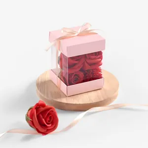 Scatola regalo rosa trasparente con fiocco e rose rosse su vassoio di legno decorativo
