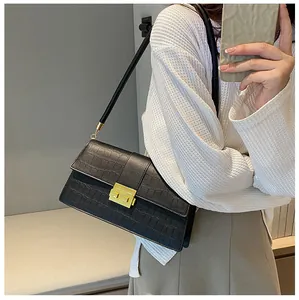 Detail of black crocodile texture shoulder bag with golden metal lock on a model