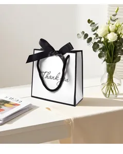 Minimalist white gift bag with black trim, silk bow, and Thank You script on wooden table