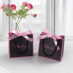 Close-up of black gift bags with pink silk bows and handwritten Thank You script