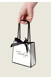 Detail of small white gift bag with black bow and Thank You text held by hand