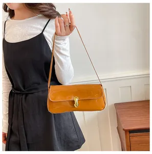 Detail view of brown patent leather baguette bag with gold buckle on a model