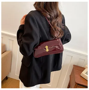 Close-up of wine red patent leather bag with gold geometric buckle worn on shoulder
