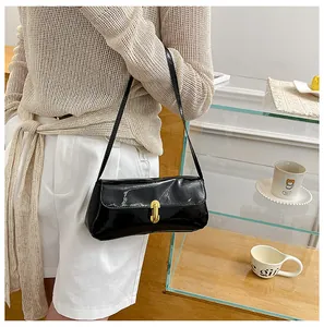 Lifestyle shot of a black patent leather baguette shoulder bag with gold metal clasp