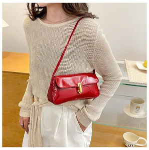 Red patent leather baguette bag with gold buckle shown on a model in a cafe setting
