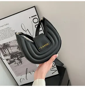 Dettaglio della borsa a sella nera trapuntata con scritte gialle e finiture dorate