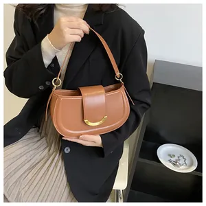 Detail of a brown leather saddle bag with a golden crescent clasp and strap hardware