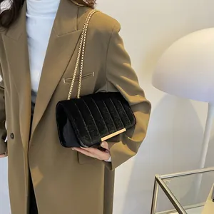 Schwarze Samt-Umhängetasche mit Steppung und Goldkette vor khakifarbenem Blazer
