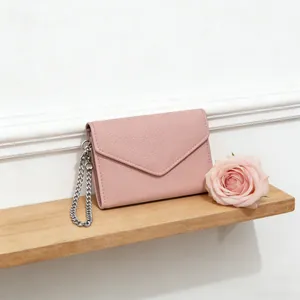 Pink lychee grain leather envelope wallet with silver chain on a wooden shelf