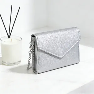 Close-up of silver lychee texture envelope wallet with elegant metal chain on marble