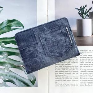 Detail view of a blue denim texture wallet with silver zipper and lifestyle props