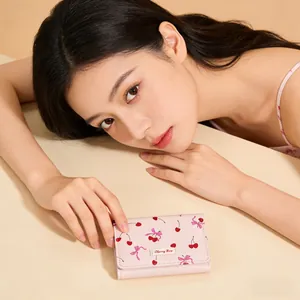 Close-up of a pink short wallet featuring sweet cherry and bow prints with a metal tag