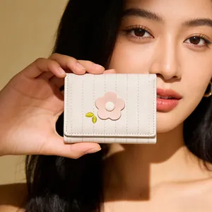 Mini portefeuille en cuir beige avec broderie florale tenu par un mannequin femme