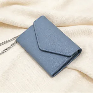 Detail view of a blue lychee texture envelope wallet with a silver chain on knit fabric