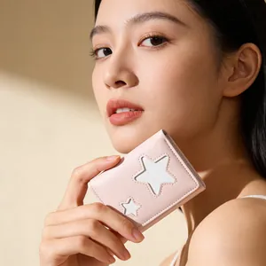 Close-up of pink star-patterned leather tri-fold wallet held in hand by a model
