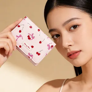 Pink trifold wallet with cherry bow print held by a hand against a beige background