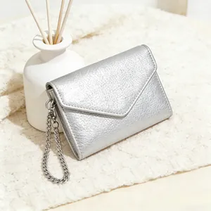 Detail of silver litchi grain mini wallet featuring a chain strap on white knit fabric