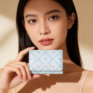 Gros plan du portefeuille bleu clair à nœud avec plaque Sweet Girl tenu par un modèle