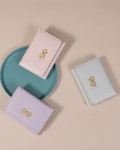 Dettaglio di portafogli rosa, viola e grigi con fiocchi dorati su una superficie beige
