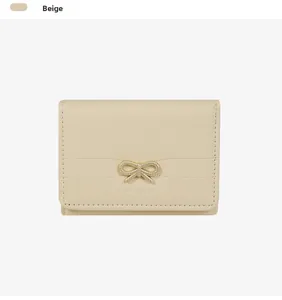 Dettaglio portafoglio in pelle beige con fiocco dorato e cuciture di precisione