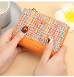 Portefeuille tissé orange tenu à la main montrant le format compact et les détails dorés