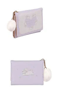 Detail view of purple trifold wallet with white rabbit prints and fuzzy pom-pom charm
