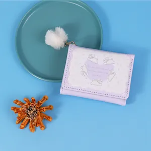 Cute lavender trifold wallet featuring cartoon rabbit graphics and a fluffy white pompom charm