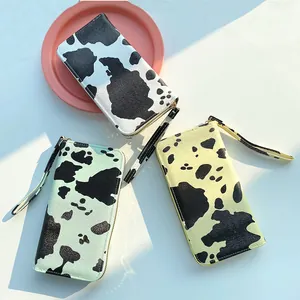 Three cow print zip-around wallets in black, mint green, and yellow with wristlet straps