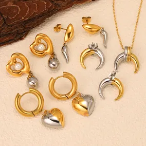 Two-tone 18K gold plated heart pearl earrings and horn necklace set on a textured surface