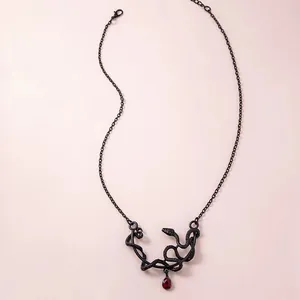 Collar de serpiente negra con gema de gota roja oscura sobre un fondo rosa suave