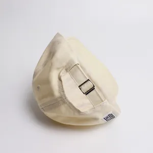 Détail de la casquette beige en coton avec boucle métallique et étiquette tissée latérale