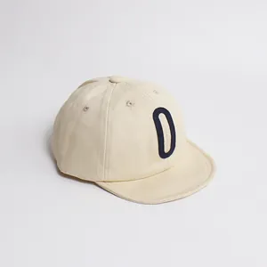 Détail de la casquette en coton crème avec écusson lettre D bleue et bord souple enfant