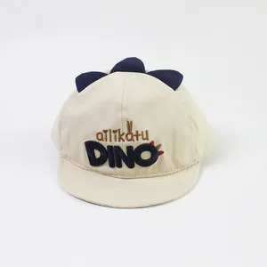 Detail of beige baby baseball cap featuring dinosaur fins and Dino embroidery