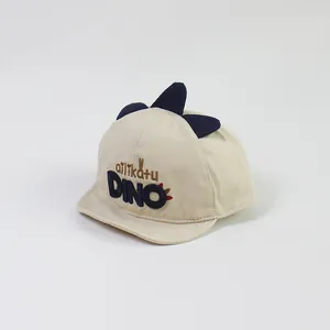 Detail of baby dinosaur baseball cap with 3D fins and embroidered dino text on beige cotton