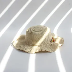 Détail d'un chapeau de paille pour enfant avec bord ondulé et trois fleurs décoratives