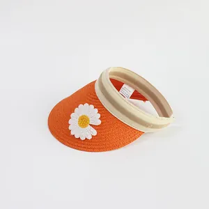 Close-up of bright orange straw sun hat featuring white daisy accents and woven texture