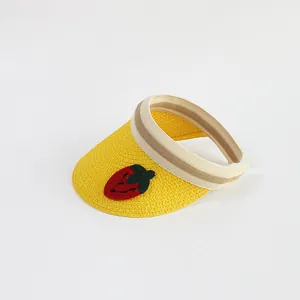 Detail of yellow straw sun visor with red strawberry embroidery and striped elastic band