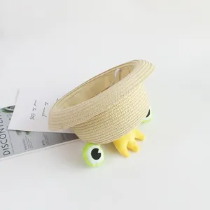Detail of straw sun hat featuring plush frog eyes, small crown and elastic wind strap