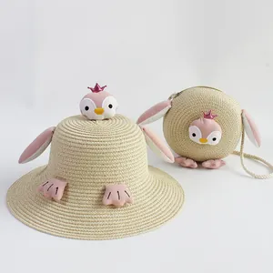 Detalle de conjunto de sombrero y bolso de paja para niños con pingüino y corona rosa