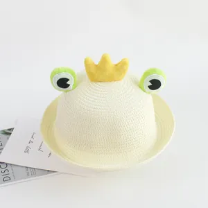Close-up of children's straw hat with frog eyes and a yellow crown on white background
