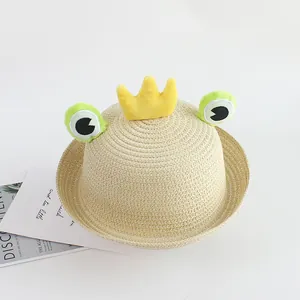 Detail of hand-woven straw hat featuring cartoon frog eyes and yellow plush crown decor