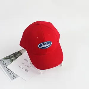 Detail of red cotton kids baseball cap with blue oval patch and white embroidery