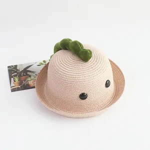 Detalle de un sombrero de paja rosa para niños con decoraciones de dinosaurio verde