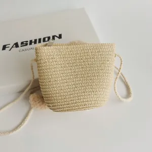 Detail of a straw mini crossbody bag featuring woven texture and pompom charm